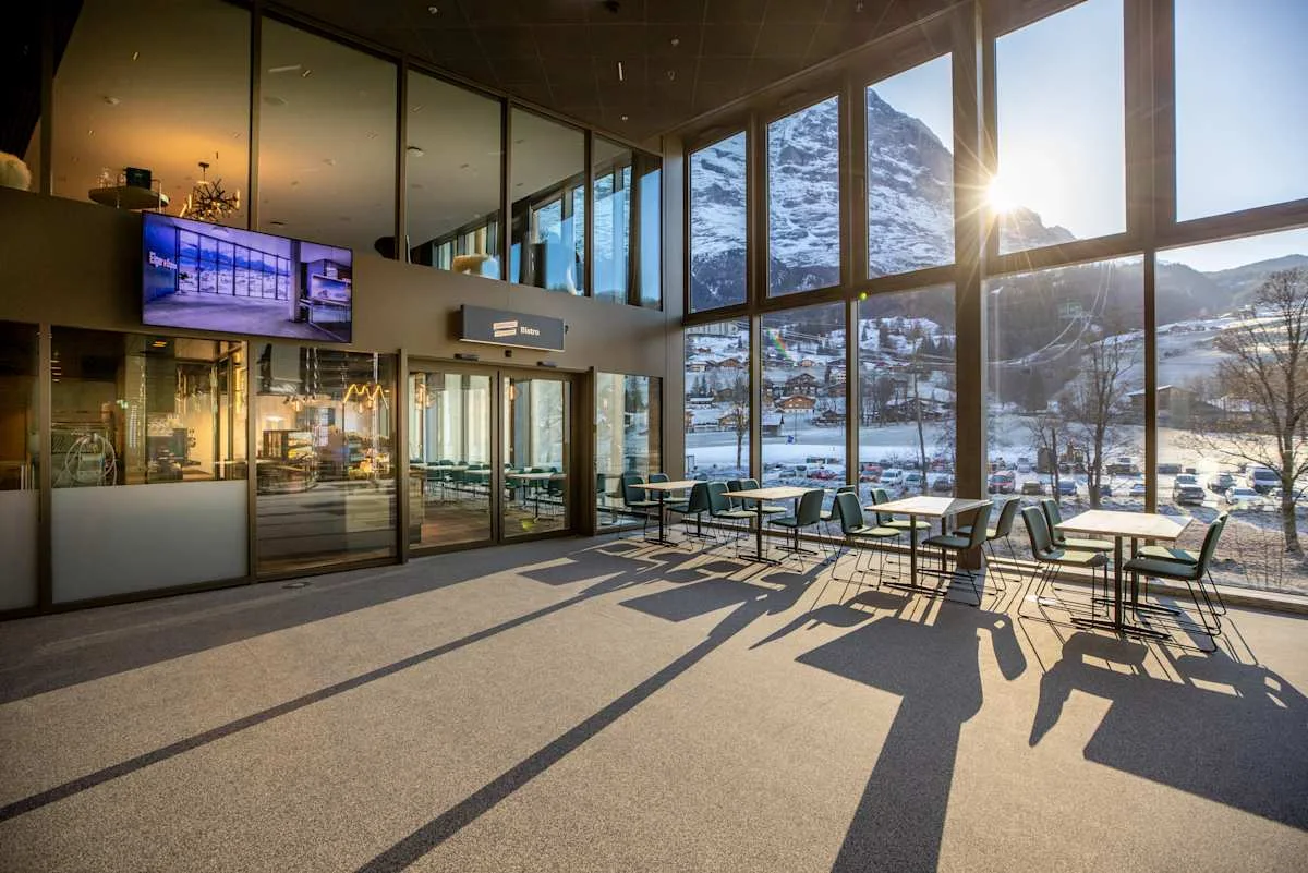 Seating area of the bistro at Grindelwald Terminal with panoramic windows overlooking the Eiger in the low evening sun.
