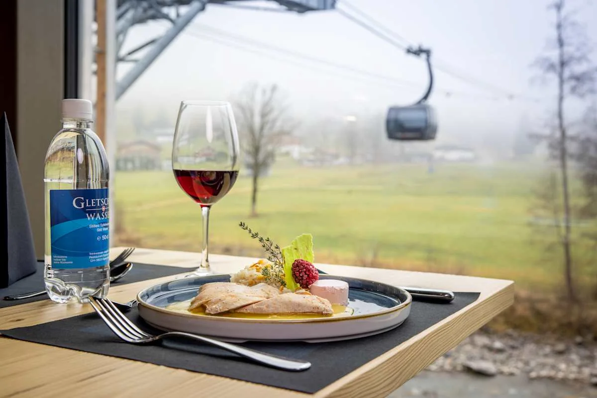 Plated meal with red wine and a view of an Eiger Express gondola.