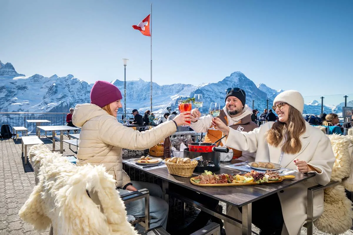 Three people toasting on the terrace of Berggasthaus First in winter